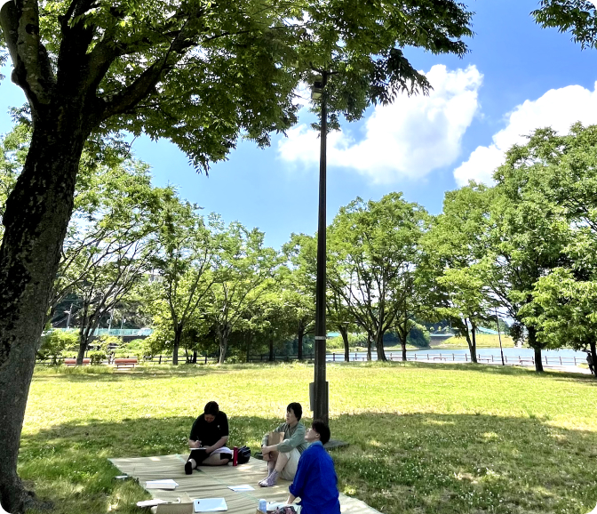 青空の下、木陰でワークを行う人々の様子